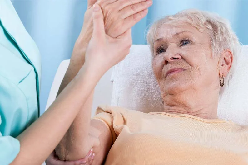 Doctor works on movement of patients arm while she lays in bed