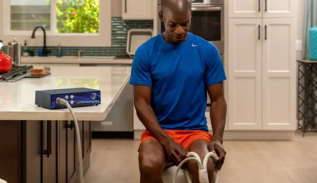 Man applying TeslaFit PEMF Butterfly Coil to his knee for treatment