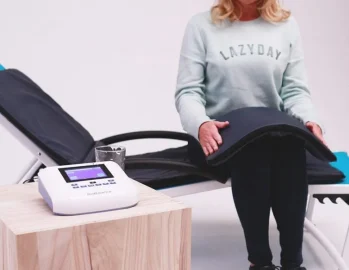 Woman sitting next to BioBalance PEMF Machine while using the mat and pillow