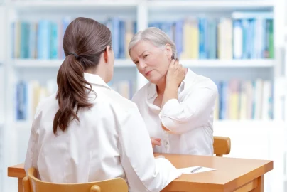 Woman rubs her neck and talks to doctor about problems she is having