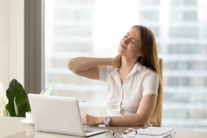 Woman rubs her neck in pain while she sits at computer and works