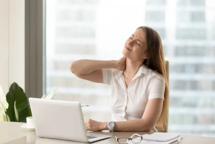 Woman rubs her neck in pain while she sits at computer and works